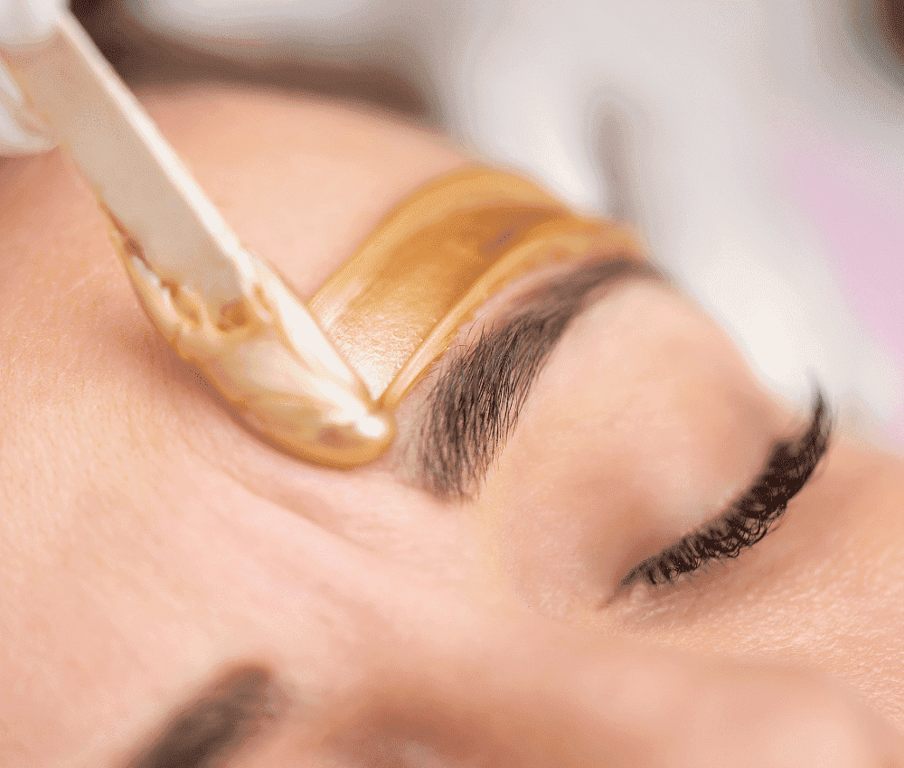 Eyebrow being shaped with golden wax strip during a beauty treatment.