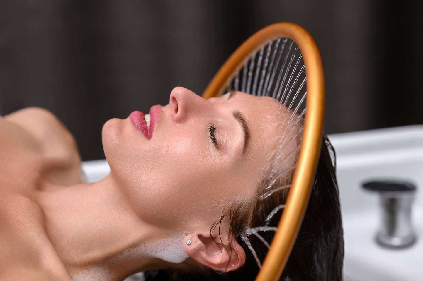 Woman enjoying a relaxing hair wash under a round shower head at a salon.