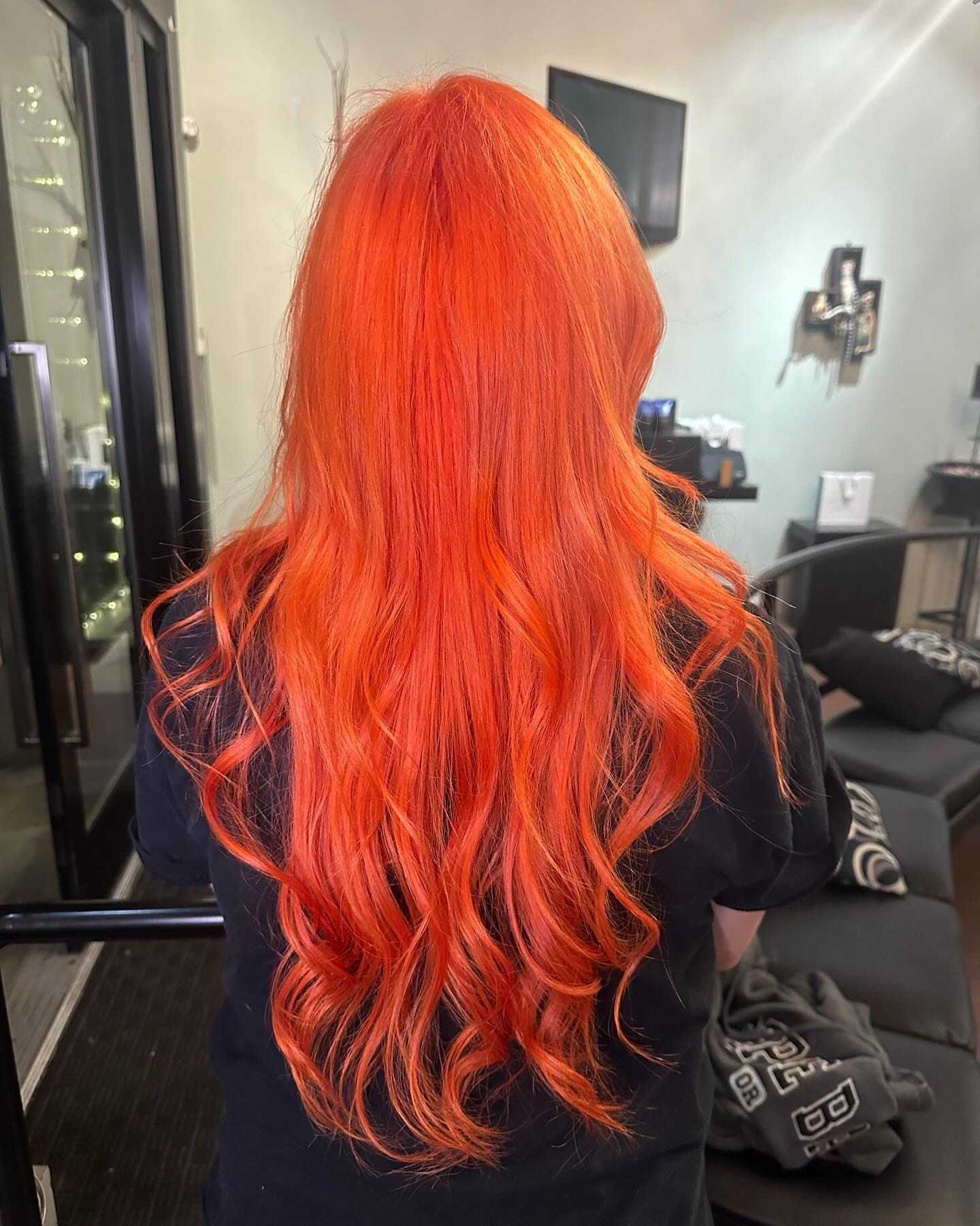 Bright orange-red hair with loose waves, viewed from behind in a salon setting.