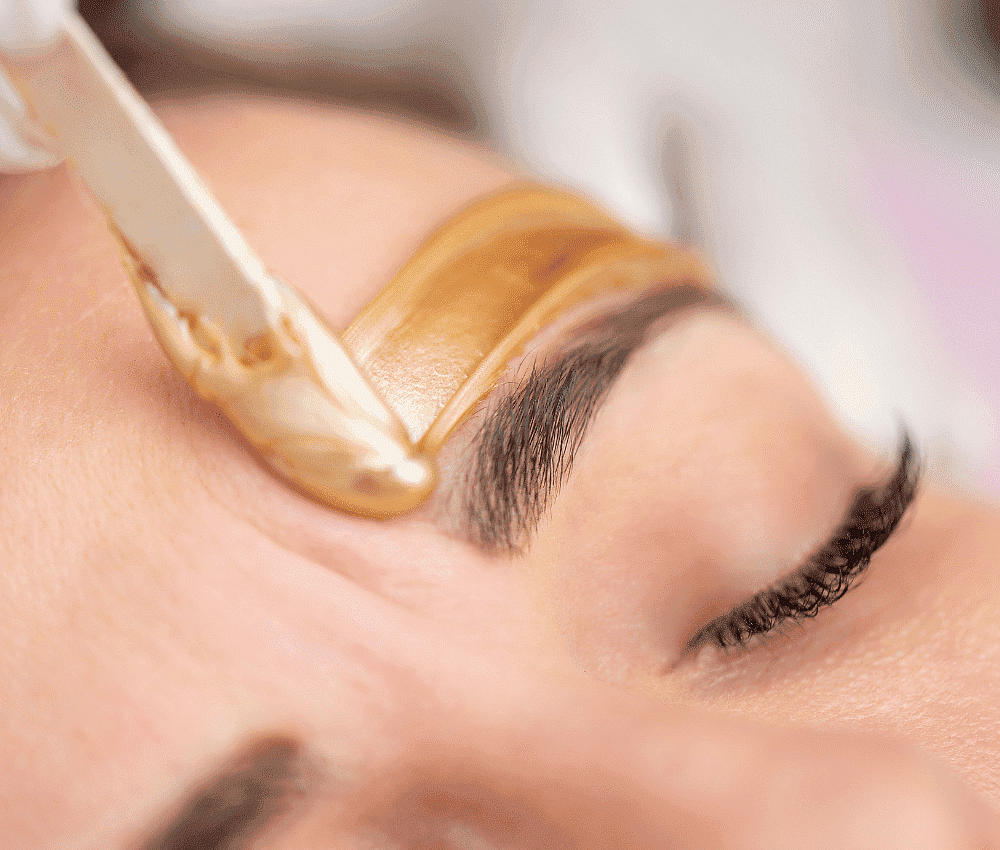 Eyebrow being shaped with golden wax strip during a beauty treatment.